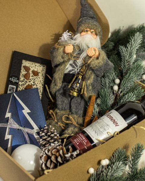 Setul cadou Moș Crăciun cu jucărie decorativă Moș Crăciun, vin, ciocolată cu migdale, jucării de brad și conuri, într-o cutie kraft